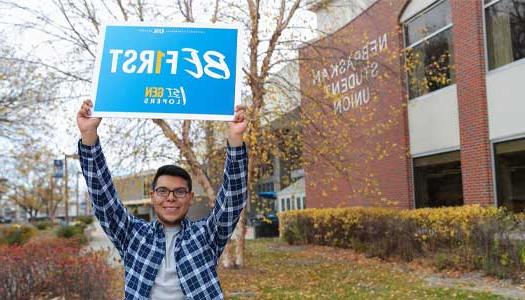 a first-generation student holds up a be first sign outside the student union